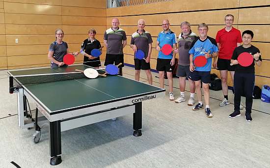 Neun Mitglieder der Tischtennis-Abteilung mit Lenkballschlgern und Tischtennisplatte.